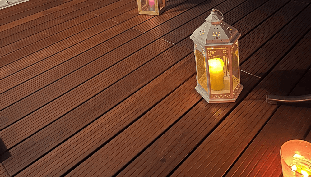Stimmungsvolle Szene auf einer gepflegten Bambus-Terrasse mit schmaler Riffelung. Mehrere dekorative Laternen mit brennenden Kerzen sorgen für warmes Licht. Die natürliche Holzoptik der Terrassendielen erinnert an Bangkirai, ist jedoch eine nachhaltige Bambus-Alternative.