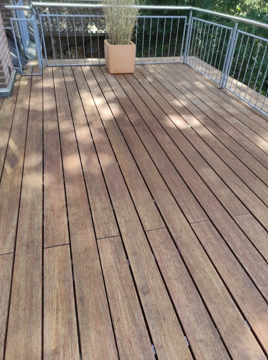 Vorher-Nachher-Vergleich einer Holzterrasse mit Edelstahlgeländer. Links sind verwitterte, graue Terrassendielen vor der Reinigung oder Pflege zu sehen, rechts dieselbe Terrasse nach der Aufbereitung mit deutlich aufgefrischter, warmbrauner Holzoberfläche. Die Terrasse befindet sich an einem Wohnhaus und ist von Bäumen umgeben.