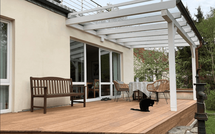 Moderne Terrasse mit Closeddecking ambooo Bambus Terrassendielen in warmem Holzton, überdacht von einer weißen Pergola, mit Sitzbank, Esstisch und Stühlen; ideale Kombination aus Langlebigkeit, Design und natürlicher Optik