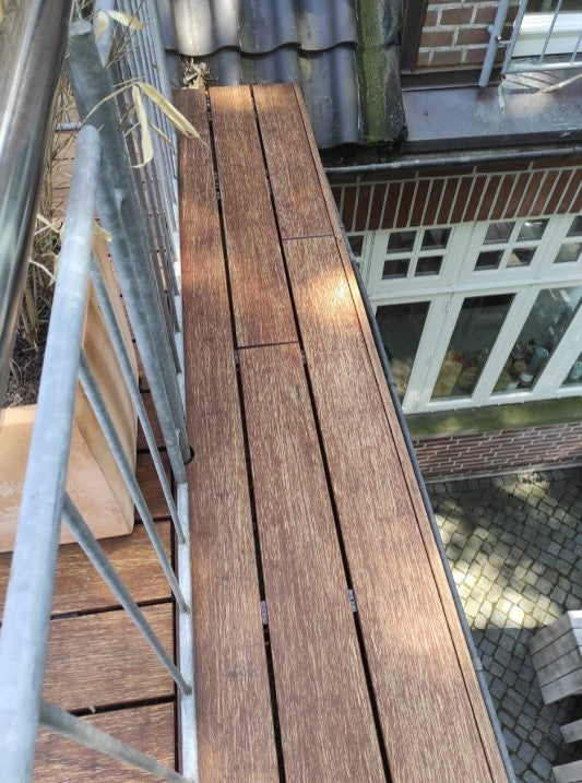 Blick entlang eines Balkonbodens aus Holz nach der Reinigung. Nach der Behandlung mit dem Anti-Belag-Reiniger,  wirkt der Belag gleichmäßig sauber und frei von Algenbewuchs. 