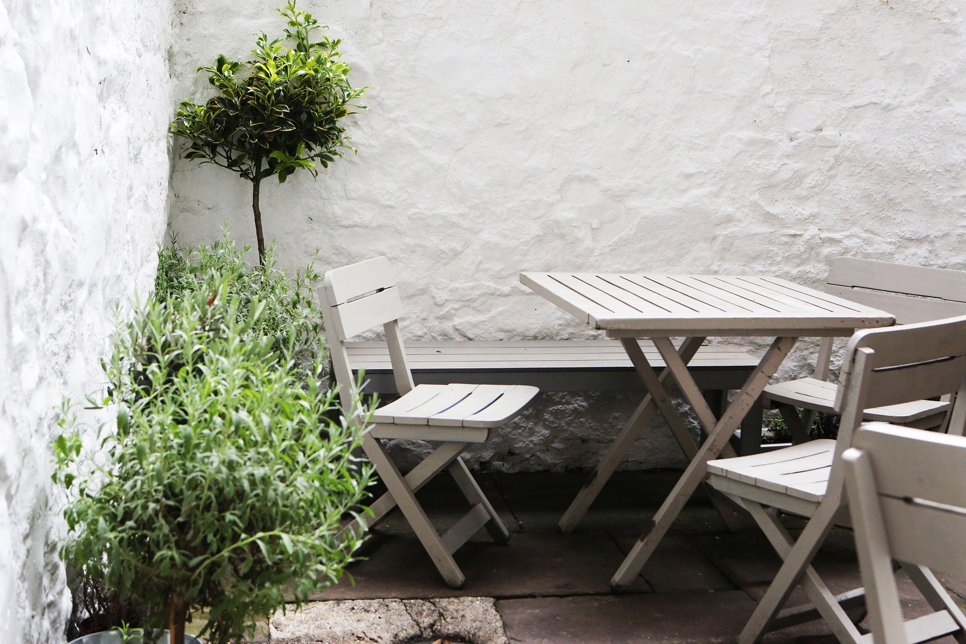 Gemütliche Bambusterrasse in einem kleinen Innenhof mit Gartenmöbeln und mediterraner Bepflanzung an weißer Steinwand.
