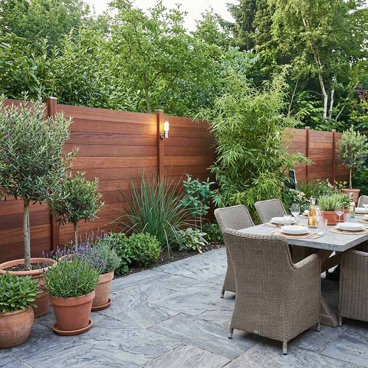 Eine AMBOOO Zaunanalge im Sommer auf Steinterrasse mit gedeckten Gartentisch.