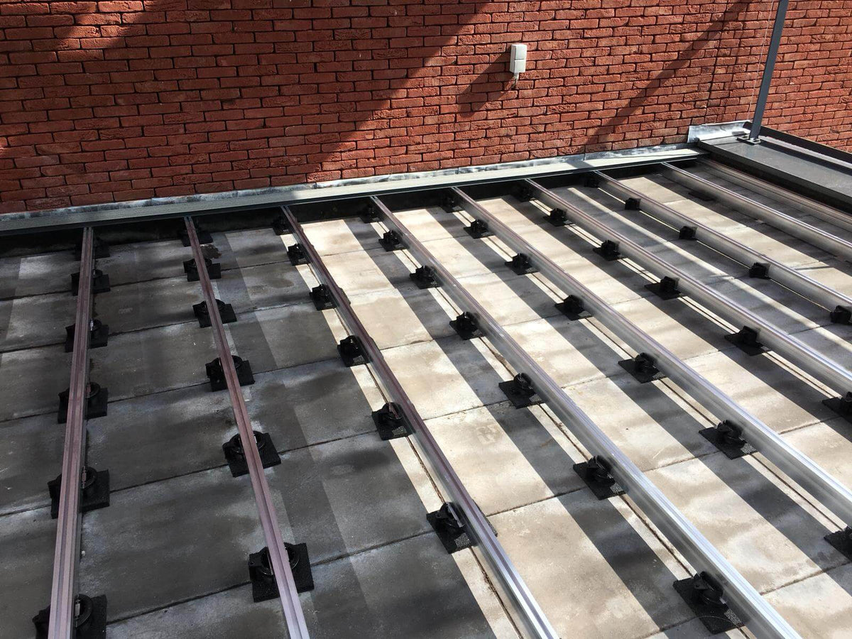 Moderne Terrassen-Unterkonstruktion mit Aluminiumprofilen und höhenverstellbaren Stelzlagern auf Plattenbelag. Die stabile und langlebige Konstruktion bildet die Grundlage für eine fachgerecht verlegte Terrasse und sorgt für optimale Belüftung sowie exakte Höhenausrichtung.