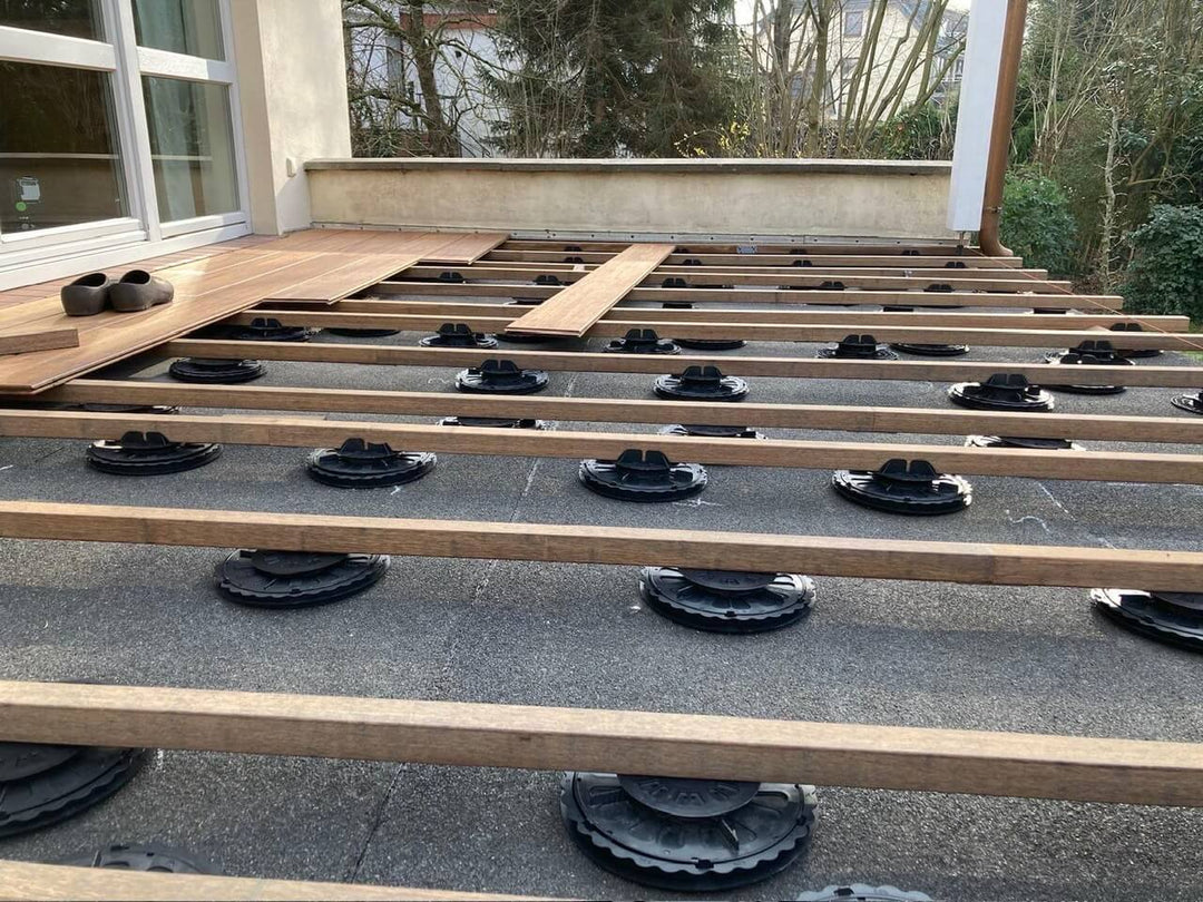 Terrassenunterkonstruktion aus Bambus auf höhenverstellbaren Stelzlagern während der Verlegung von Terrassendielen. 