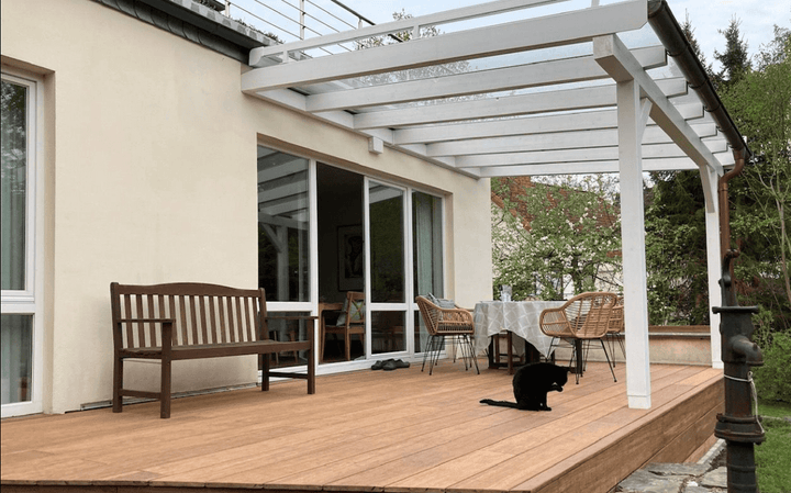 Moderne Terrasse mit Closeddecking ambooo Bambus Terrassendielen in warmem Holzton, überdacht von einer weißen Pergola, mit Sitzbank, Esstisch und Stühlen; ideale Kombination aus Langlebigkeit, Design und natürlicher Optik