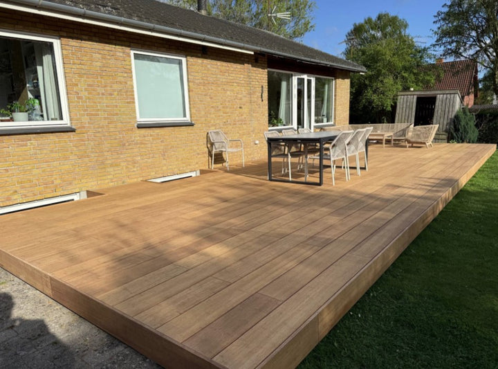 großzügige Terrasse erstellt mit ambooo closed decking Terrassendielen in natürlicher Holzoptik, aussgestattet mit moderenen Essbereich und Loungemöbeln, vor einem Einfamilienhaus mit gelber Klinkerfassade.