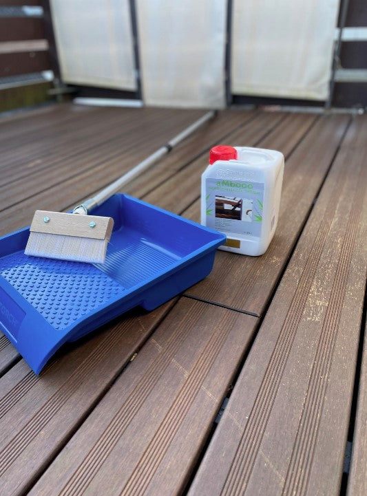 Farbwanne, Flächenstreicher und Terrassenöl stehen auf einer Bambusterrasse bereit, um die Dielen zu reinigen und mit Pflegeöl zu behandeln.