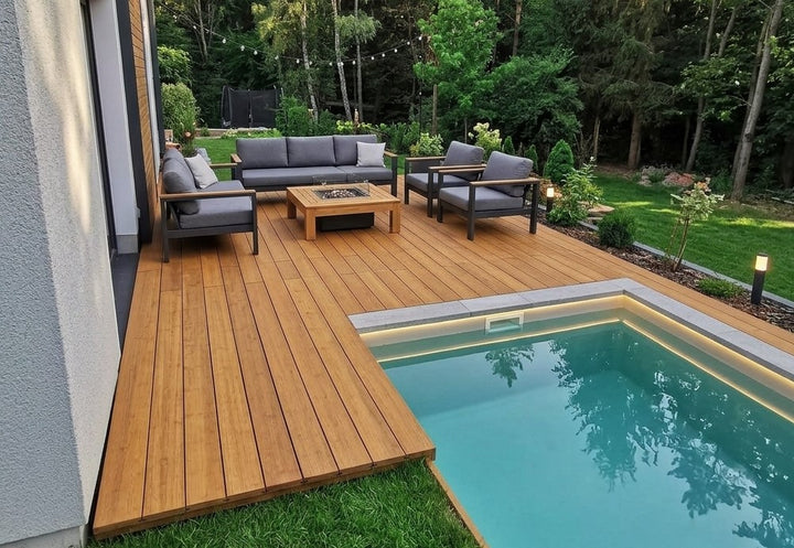 Großzügige Poolterrasse aus Campoverde Bambus-Terrassendielen mit Loungemöbeln, Feuertisch und beleuchtetem Pool am Wohnhaus.