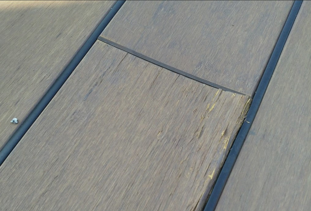 Nahaufnahme von Bambus-Terrassendielen mit sichtbarer Beschädigung an einer Diele. Die Oberfläche weist Absplitterungen und Verformungen aufgrund einer dauerhaften Durchfeuchtung auf.