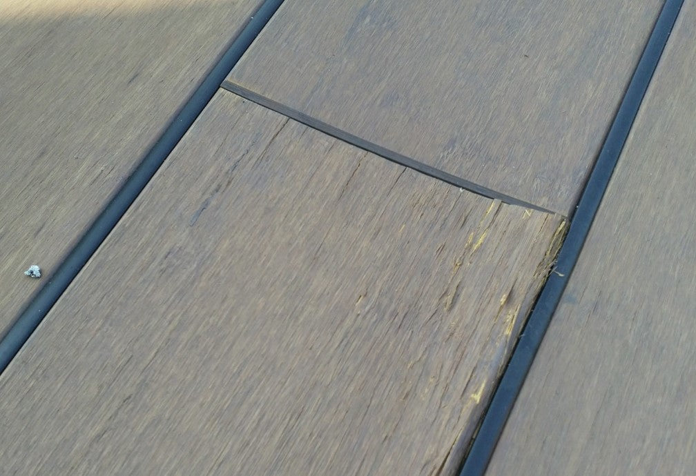 Nahaufnahme von Bambus-Terrassendielen mit sichtbarer Beschädigung an einer Diele. Die Oberfläche weist Absplitterungen und Verformungen aufgrund einer dauerhaften Durchfeuchtung auf.