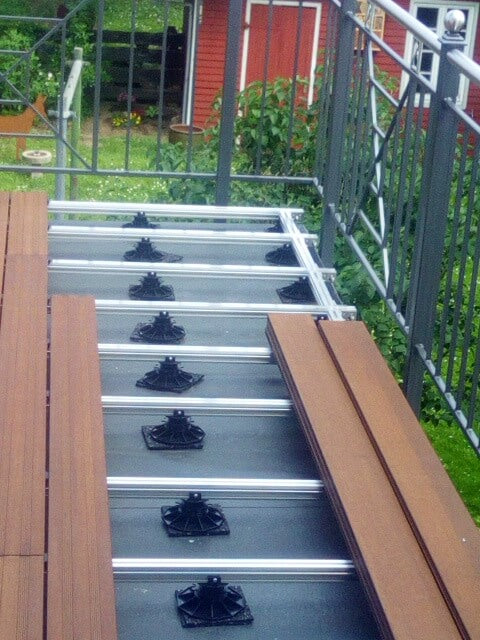 Bambus Terrassendielen werden auf einer Aluminium-Unterkonstruktion mit höhenverstellbaren Stelzlagern verlegt. Das Bild zeigt den Baufortschritt einer erhöhten Terrasse mit Geländer.