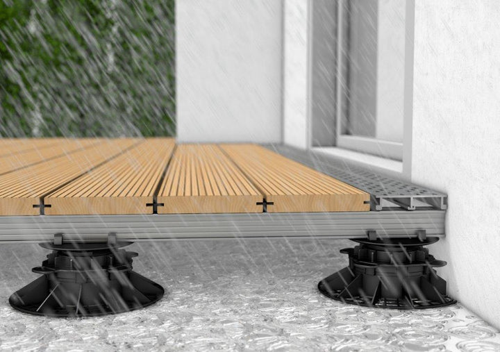 Technische Darstellung einer Terrassen-Drainage am Wandanschluss unter Holzdielen auf Stelzlagern.